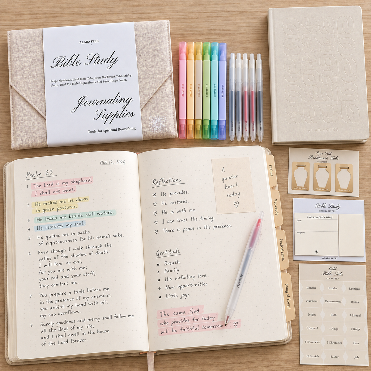 An Alabaster Co. designed Bible study and journaling kit arranged on a light wood surface, including an open journal with handwritten Bible verses and notes, a closed journal, a set of colored pens, sticky notes, cards, and a branded Bible Study packet.