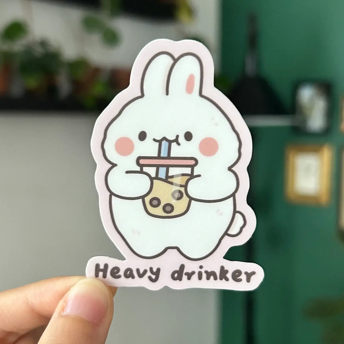 Sticker of a cartoon rabbit holding a cup with 'Heavy drinker' text, held by a hand.
