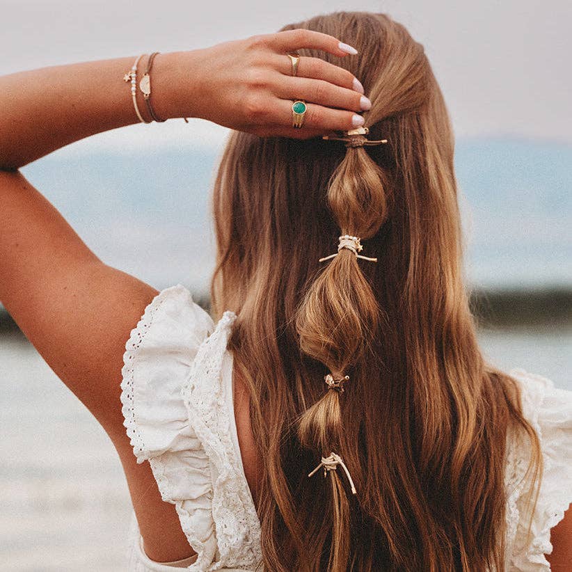 Woman with braided hair holding a braid, wearing a white lace top, with a blurred natural background.