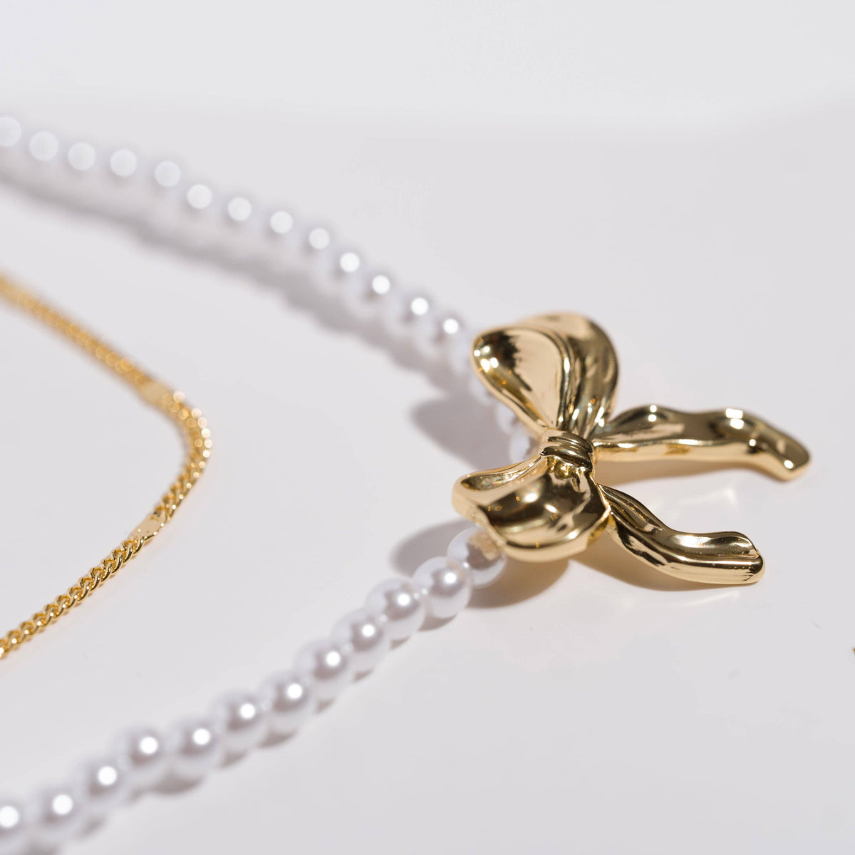 Gold bow-shaped pendant on a white pearl necklace against a light background