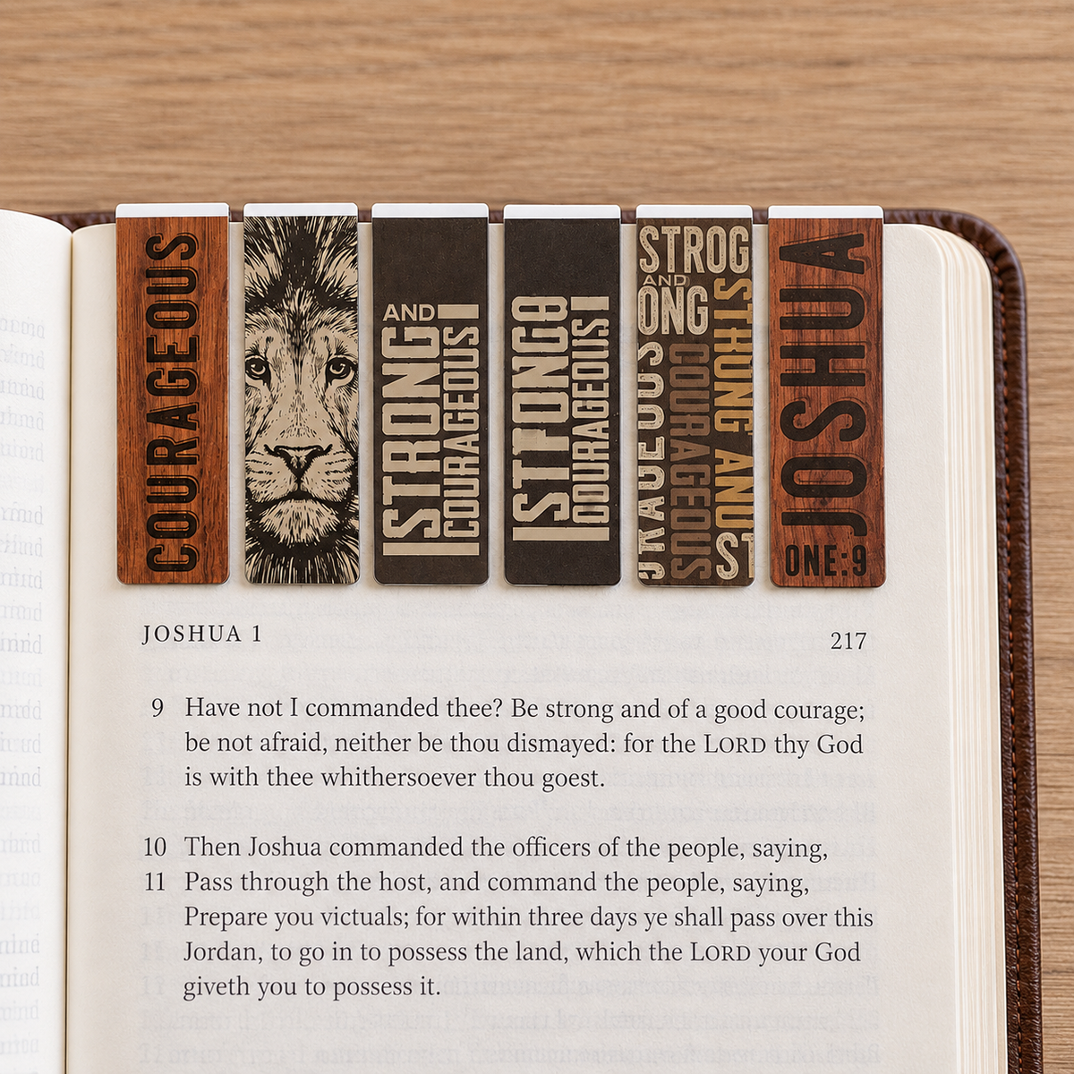 Six magnetic bookmarks with engraved Bible verses and a lion illustration, shown inserted into an open Bible on a light wood surface, by Christian Art Gifts.