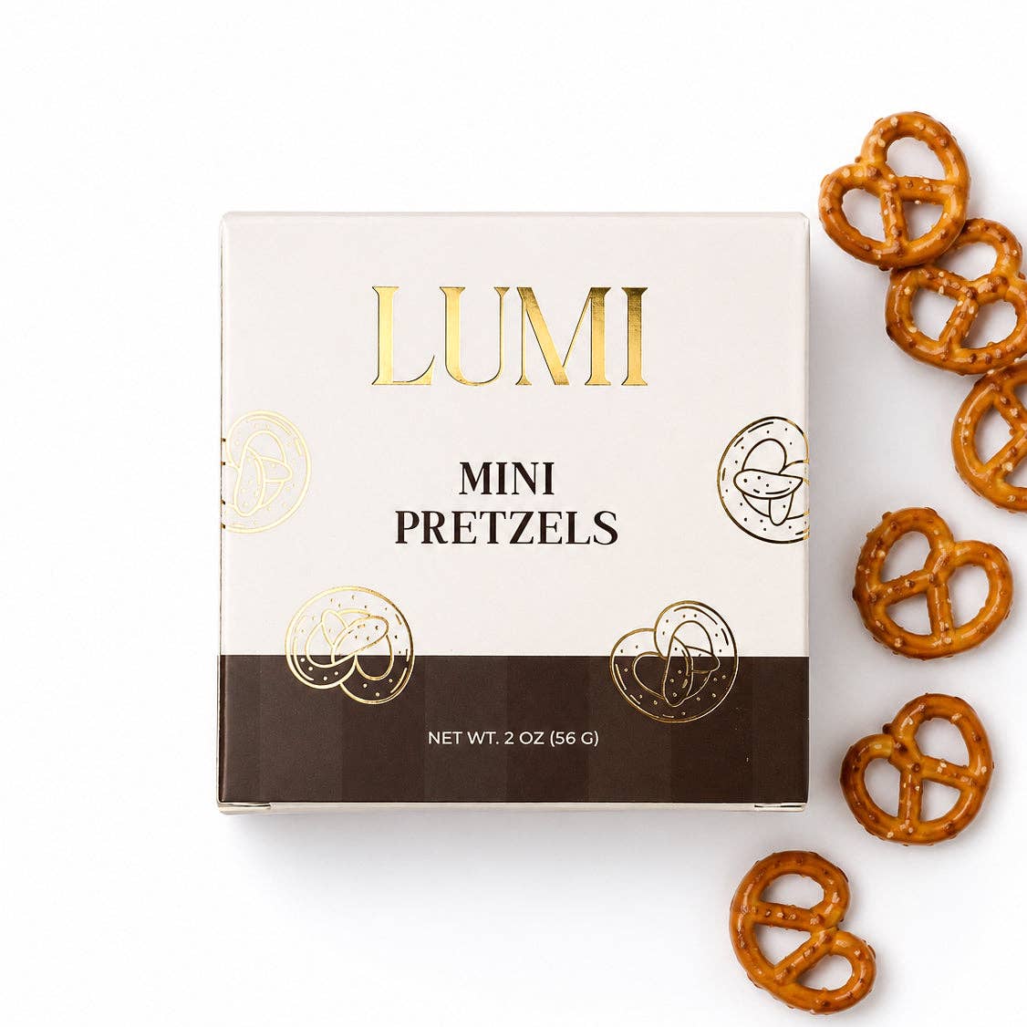 A square white and dark brown box of LUMI Mini Pretzels with gold foil lettering, shown on a white background with several pretzels scattered to the right.