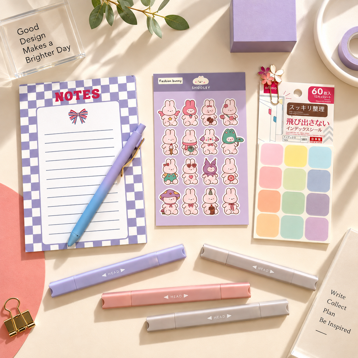 A styled flat-lay of stationery items on a warm beige surface: a purple-and-white checkered notepad, a purple blue pen, a sheet of pastel bunny stickers, a pack of multicolor sticky notes, three pastel highlighters, and binder clips. Decorative leaves, a small vase, and other props surround the products. Gift box set curated by Amazing Robin Gifts.