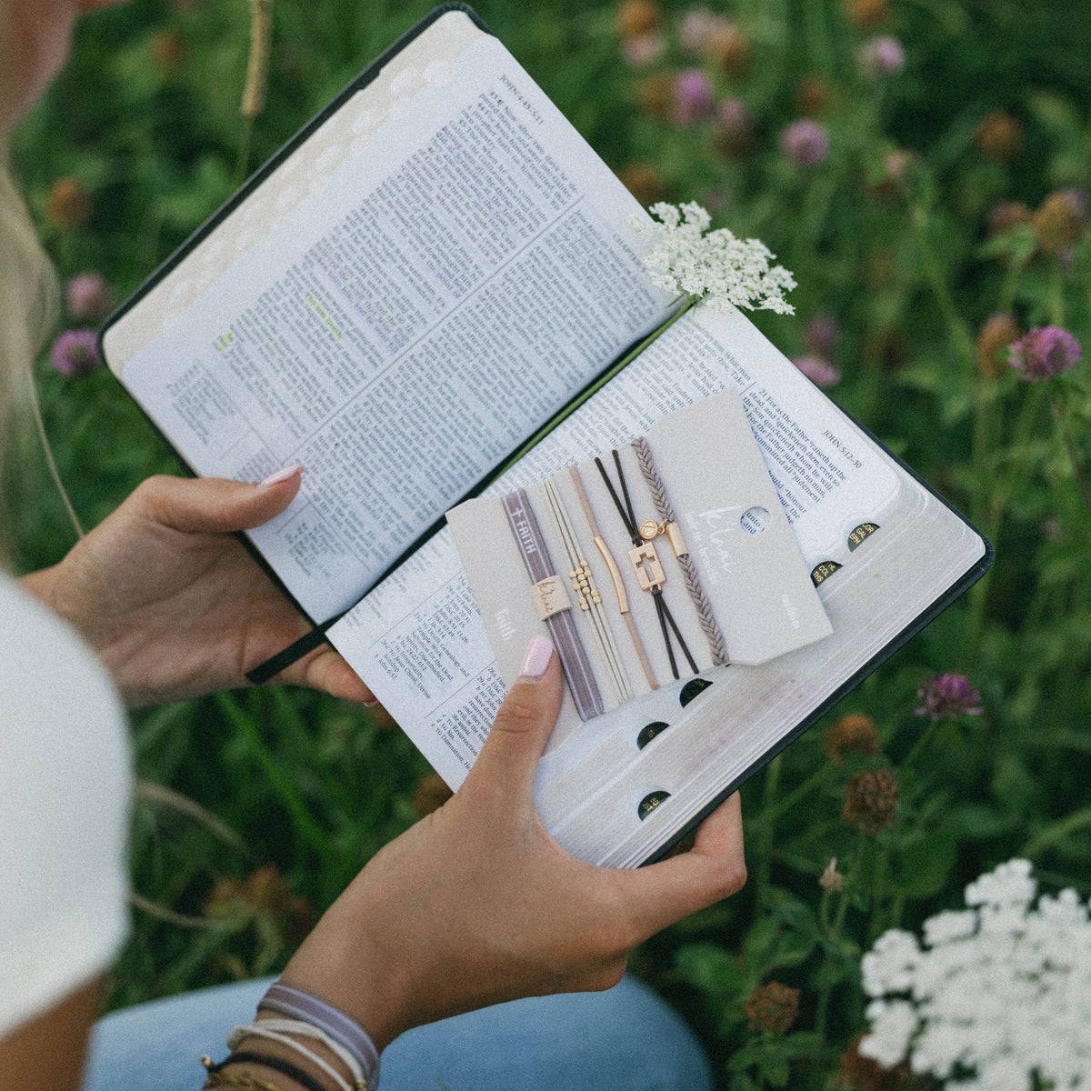 Person holding an open book with jewelry illustrations in a natural setting